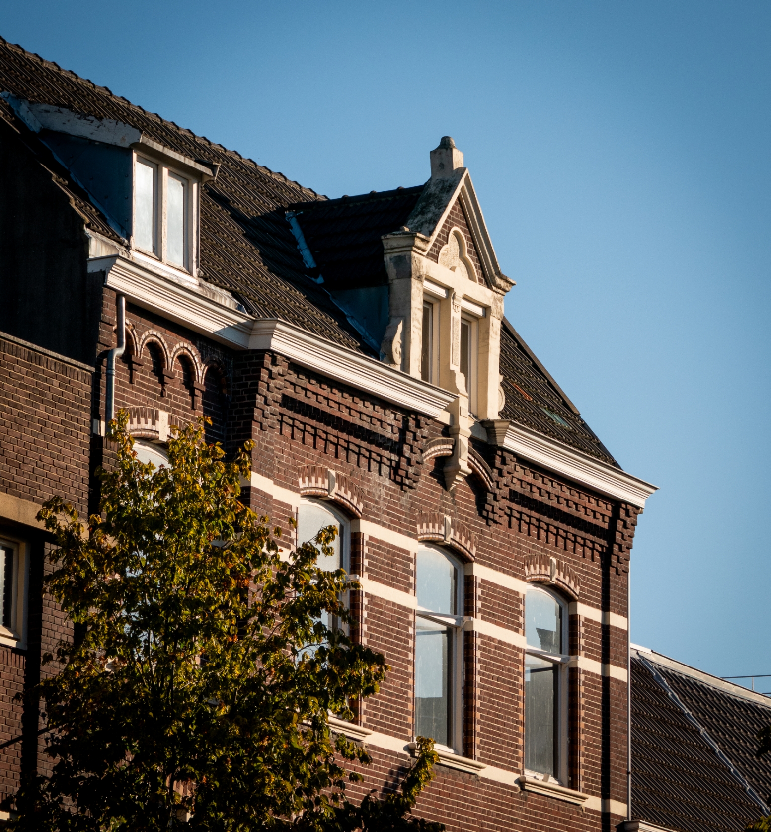 Historisch bakstenen gebouw met siergevel en dakkapel tegen een heldere blauwe lucht